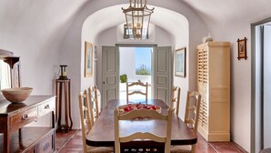 A dining room with a long wooden table, chairs, and a chandelier. There is a door leading outside and a cabinet on the right. - Nautilus,3 bedroom character villa with outdoors jacuzzi and fantastic sea views (Firostefani)
