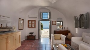 A spacious living room with a view of the sea, a large cabinet, a dining table, and a cozy seating area. - Nautilus,3 bedroom character villa with outdoors jacuzzi and fantastic sea views (Firostefani)