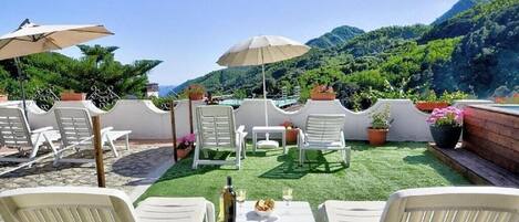 Relax on the patio with a view of lush hills, surrounded by comfortable seating and lush greenery.