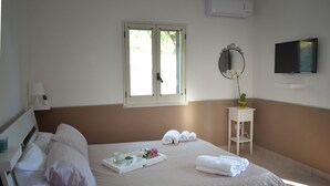 A hotel room with a bed, a bedside table with a lamp, a tray with towels and a flower, a window, a TV, and a mirror on the wall. - Villa INN Costa Casa Ravello (Tramonti)