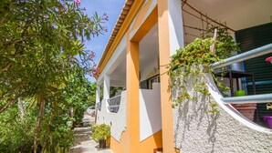 Uma casa de dois andares com fachada branca e laranja, uma varanda com vasos de plantas e uma escadaria que leva ao andar superior.