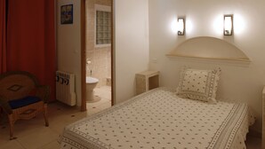 Een slaapkamer met een bed, een stoel, een radiator, een toilet en een douchehoek.