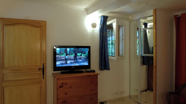 Una habitación con un armario de madera, un televisor encima, un espejo y una ventana con cortinas.