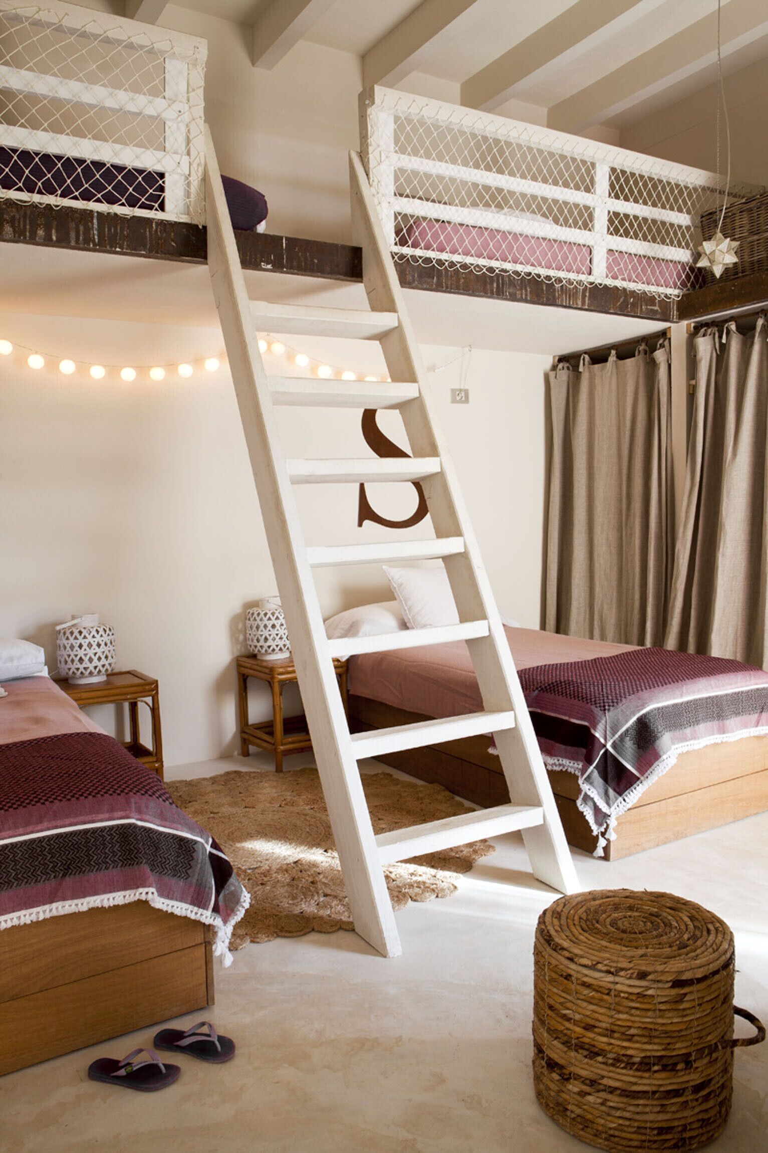 Une chambre avec un lit superposé, une échelle, deux tables de chevet et un panier en osier.