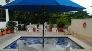 A swimming pool with a blue umbrella, white chairs, and potted plants. - Apartamentos 3-54 (San Andrés)