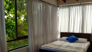 A bedroom with a bed, curtains, and a window with a view of greenery. - Apartamentos 3-54 (San Andrés)