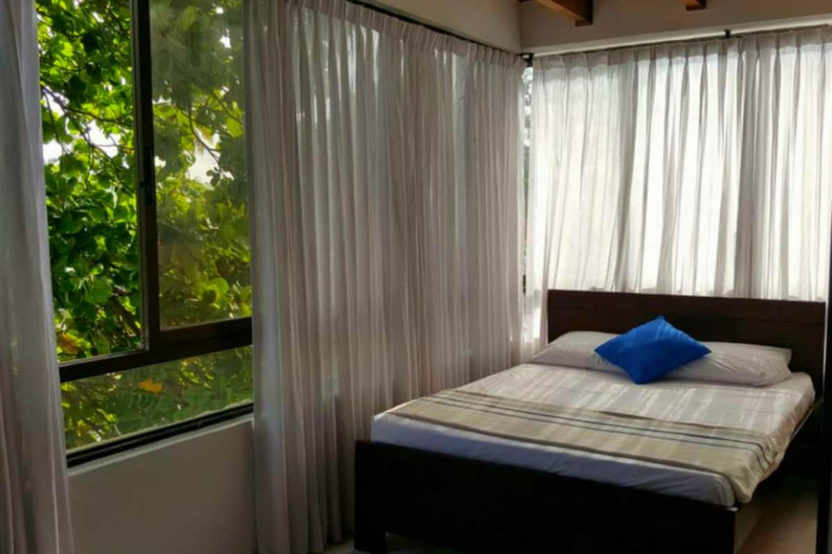 A bedroom with a bed, curtains, and a window with a view of greenery.