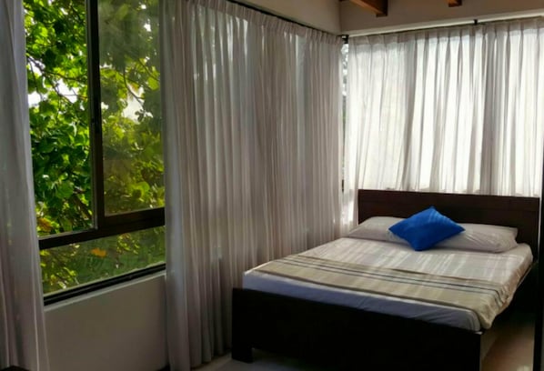 A bedroom with a bed, curtains, and a window with a view of greenery.