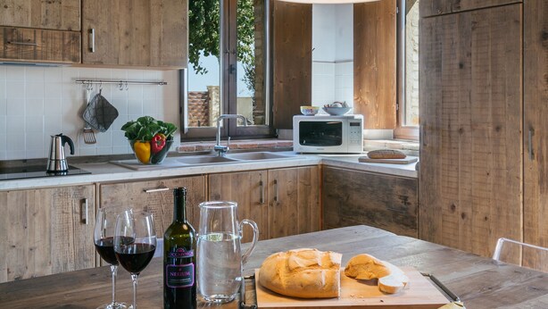 Una cocina rústica con vigas de madera, un lámpara colgante, un lavamanos, un microondas y una mesa de madera con comida y bebidas.