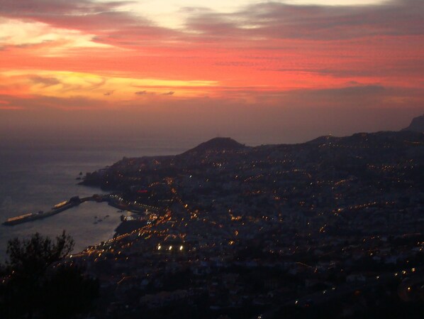 Une vue sur une ville côtière au crépuscule, avec un port bien visible et des bâtiments illuminés.
