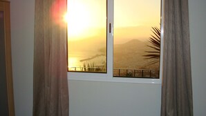 Una habitación con vista a una puesta de sol sobre un cuerpo de agua y una cadena montañosa distante.