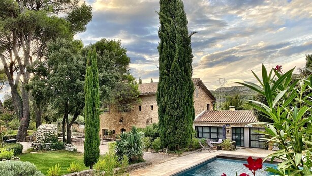 A pool surrounded by a garden with tall trees and a stone building.