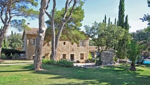A stone house with a tiled roof, surrounded by lush greenery and trees.