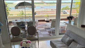 Ein Wohnzimmer mit einer Couch, Sesseln, einem Couchtisch und Blick auf den Strand durch große Fenster.