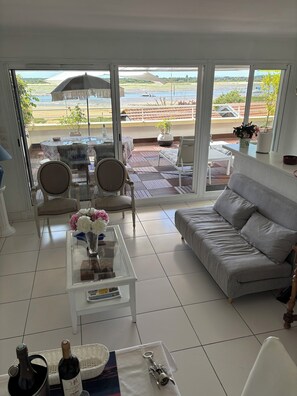 Un salon comprenant un canapé, des fauteuils, une table basse et offrant une vue sur la plage grâce à de grandes fenêtres.