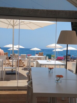 An outdoor seating area with white tables and chairs, white umbrellas, and a view of the sea. - Apartment with terrace and views of the sea, town and mountains (Calella Barcelona)