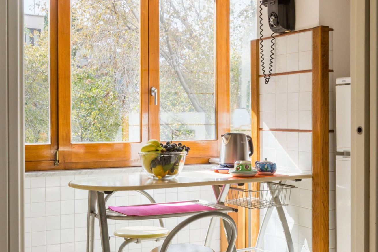 A kitchen with a window, a bowl of fruit, a kettle, and a chair.