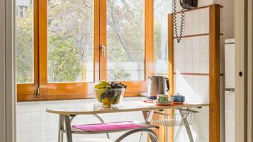 A kitchen with a window, a bowl of fruit, a kettle, and a chair.