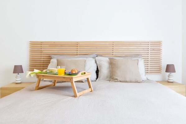 A neatly made bed with a wooden headboard, a bedside table with a lamp, and a tray with breakfast items.