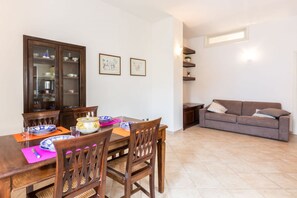 Uma área de refeições com uma mesa e cadeiras de madeira, um armário com louças e um sofá ao fundo.