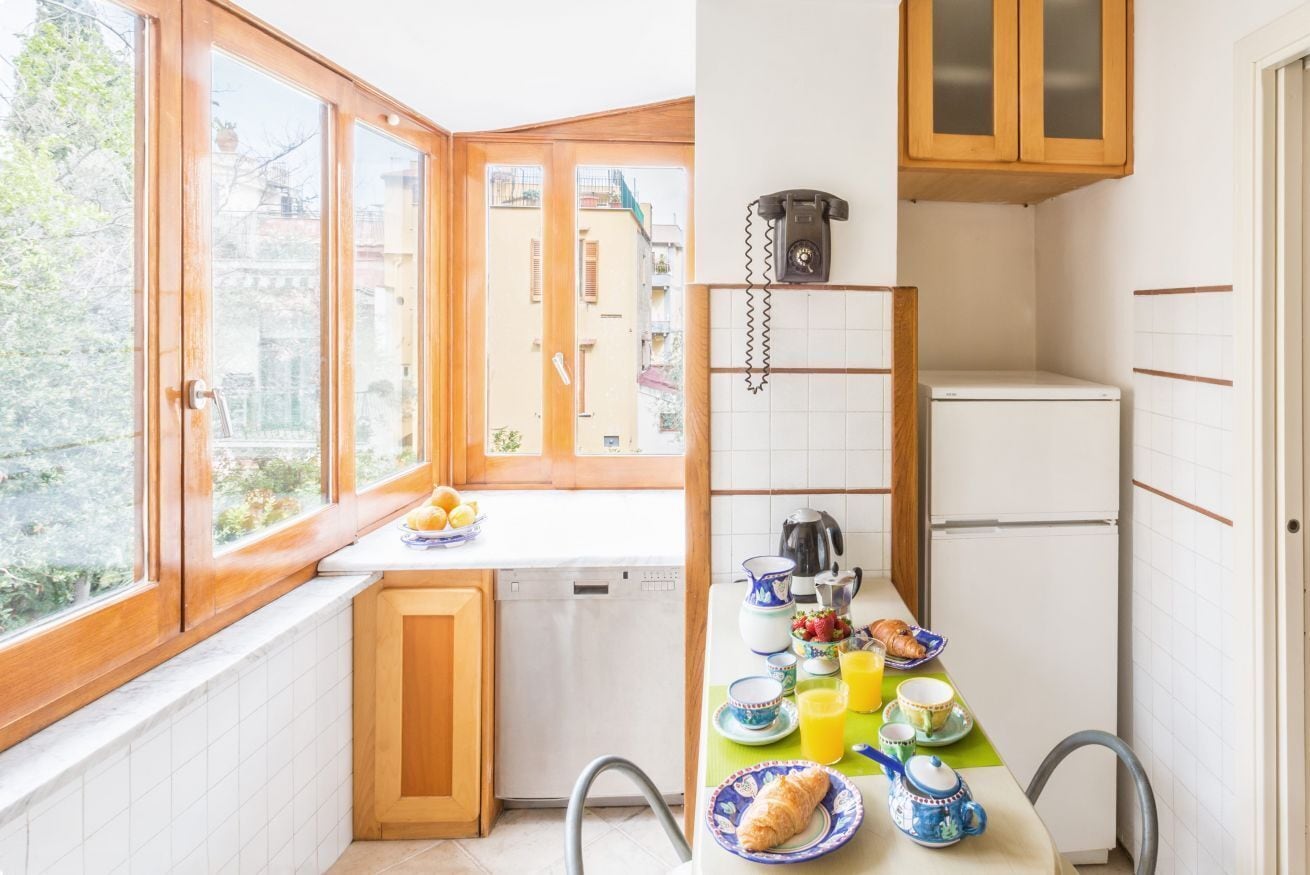 Eine Küche mit Fenster, Holzschränken, einem Kühlschrank und einem für das Frühstück gedeckten Tisch.
