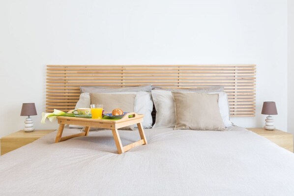 A neatly made bed with a wooden headboard, a bedside table with a lamp, and a tray with breakfast items.
