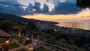 A terrace with outdoor seating and a view of a coastal city at sunset.