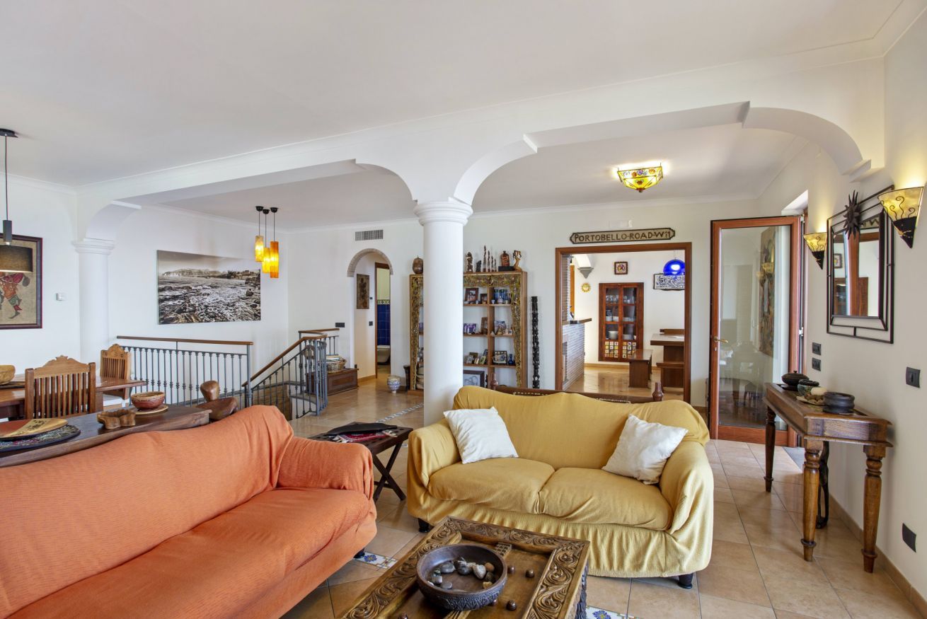 A spacious living room with a yellow sofa, an orange sofa, and a coffee table with decorative items. There is a staircase leading to another level, and a sign reading "PORTOBELLO ROAD."