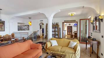 A spacious living room with a yellow sofa, an orange sofa, and a coffee table with decorative items. There is a staircase leading to another level, and a sign reading "PORTOBELLO ROAD."