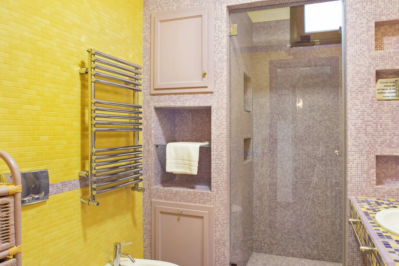 Une salle de bain avec un mur recouvert de carreaux jaunes, une douche en verre, un porte-serviettes et un lavabo.