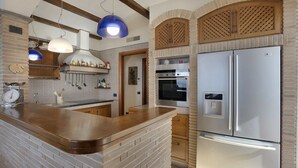 A kitchen with a brick island, stainless steel appliances, wooden cabinets, and hanging pendant lights.
