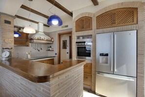 Una cocina con una isla de ladrillo, electrodomésticos de acero inoxidable, armarios de madera y lámparas colgantes.