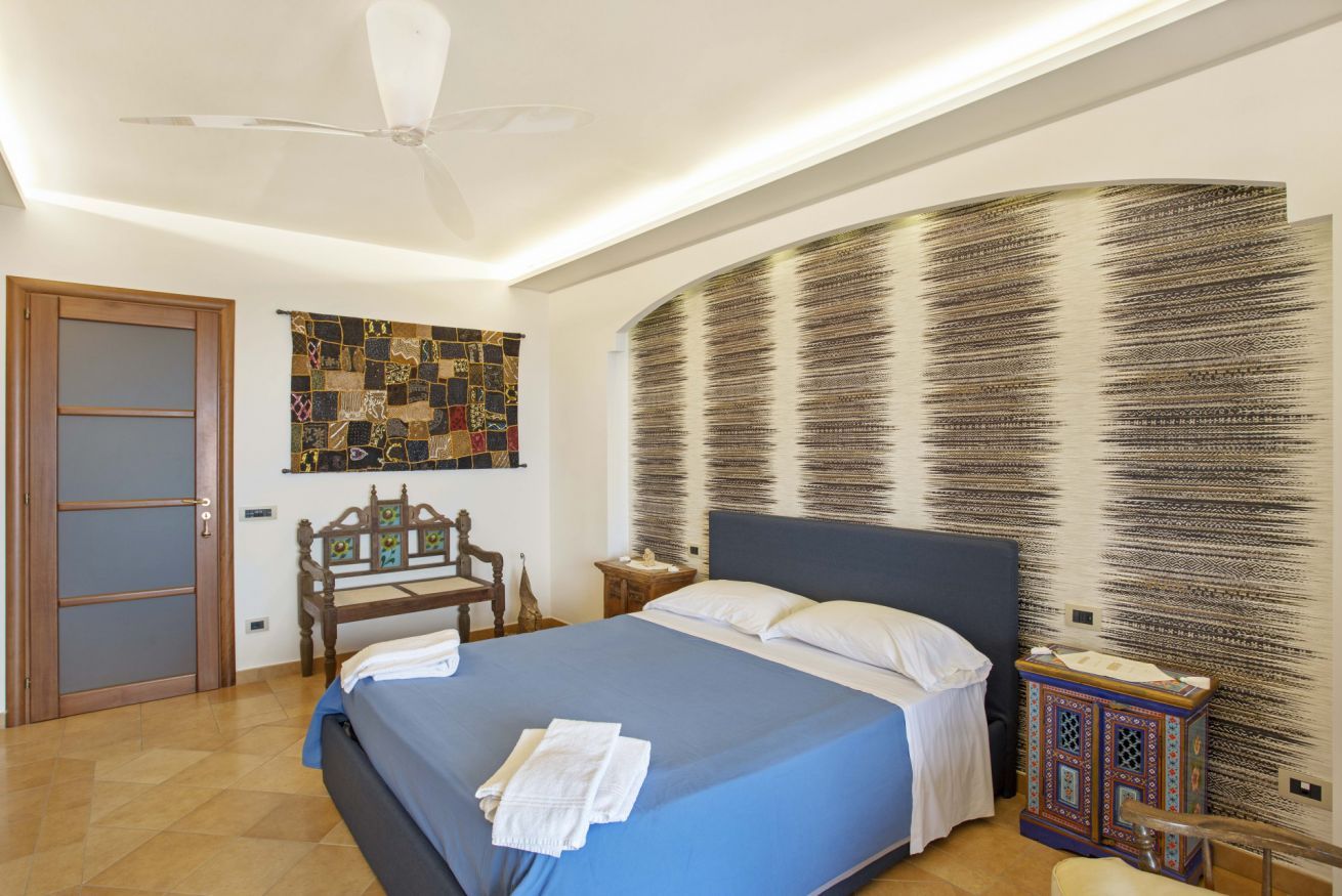 Una camera da letto con un letto, una ventola a soffitto, un'opera d'arte a parete, una panca in legno e un mobile decorativo.