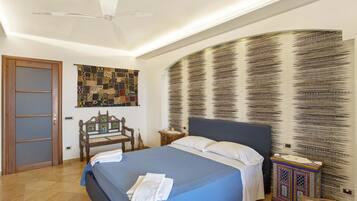 Una camera da letto con un letto, una ventola a soffitto, un'opera d'arte a parete, una panca in legno e un mobile decorativo.