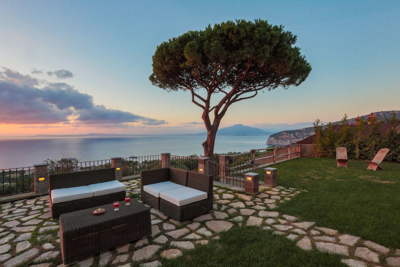An outdoor seating area with wicker furniture, a stone pathway, and a view of the sea.