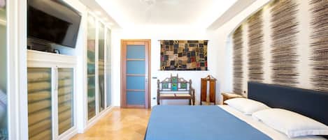 Un dormitorio con cama, ventilador de techo, televisor, banca de madera y pared con textura.