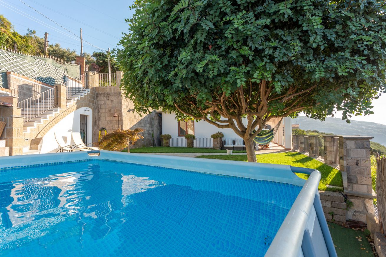 A swimming pool with a tree in the background, a stone staircase, and a white building with a door.