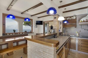 A kitchen with a central island, wooden beams, and hanging blue pendant lights. - MyExclusiveItaly - Luxury Villa with breathtaking Seaview,pool,BBQ (Sorrento)