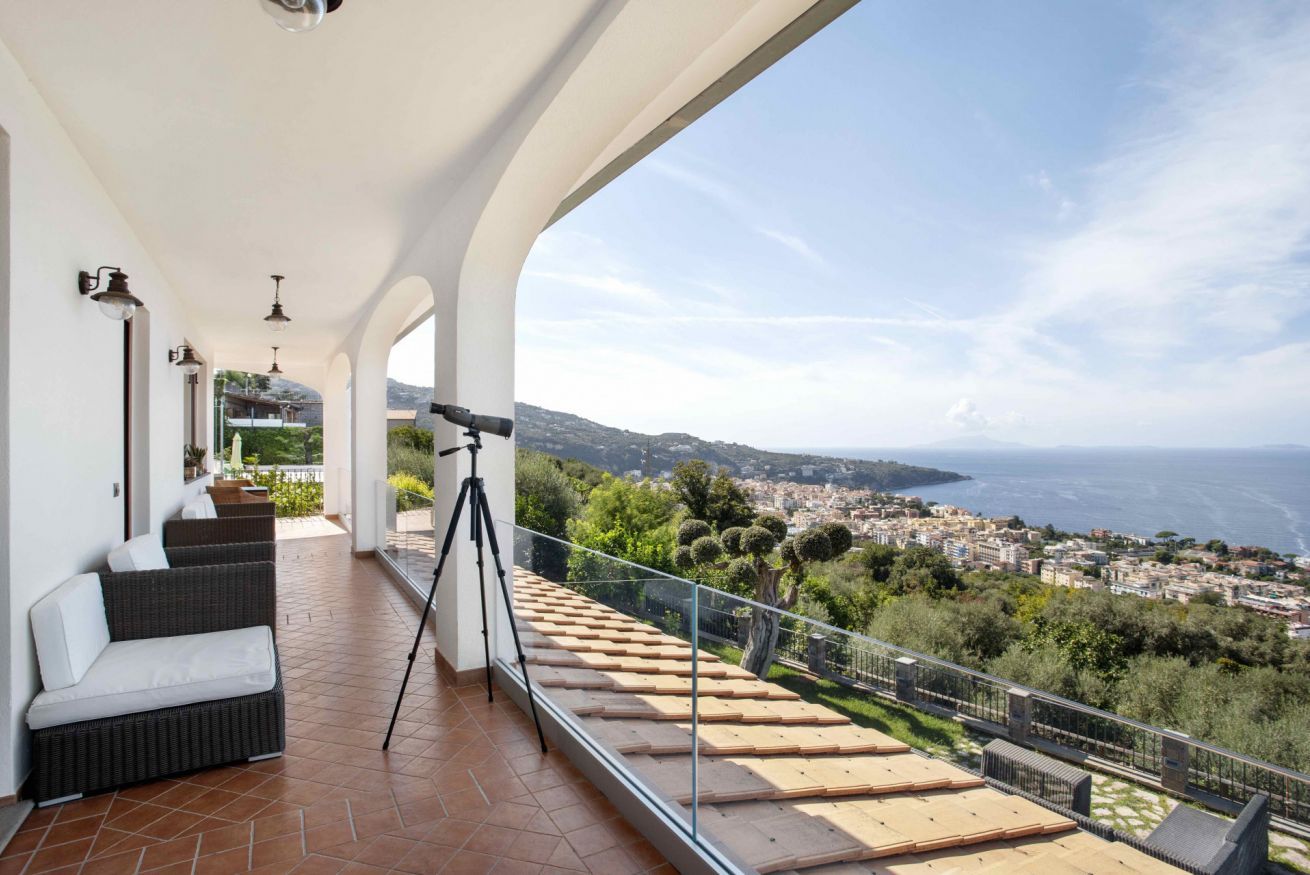 Un balcon avec un canapé, un trépied et une vue sur une ville côtière.