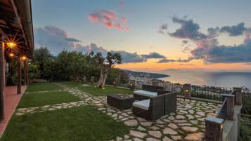 Un patio con pavimento in pietra, arredi da esterno e vista sul mare al tramonto.