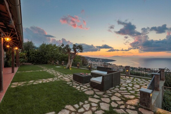 A patio with stone flooring, outdoor furniture, and a view of the sea at sunset. - MyExclusiveItaly - Luxury Villa with breathtaking Seaview,pool,BBQ (Sorrento)