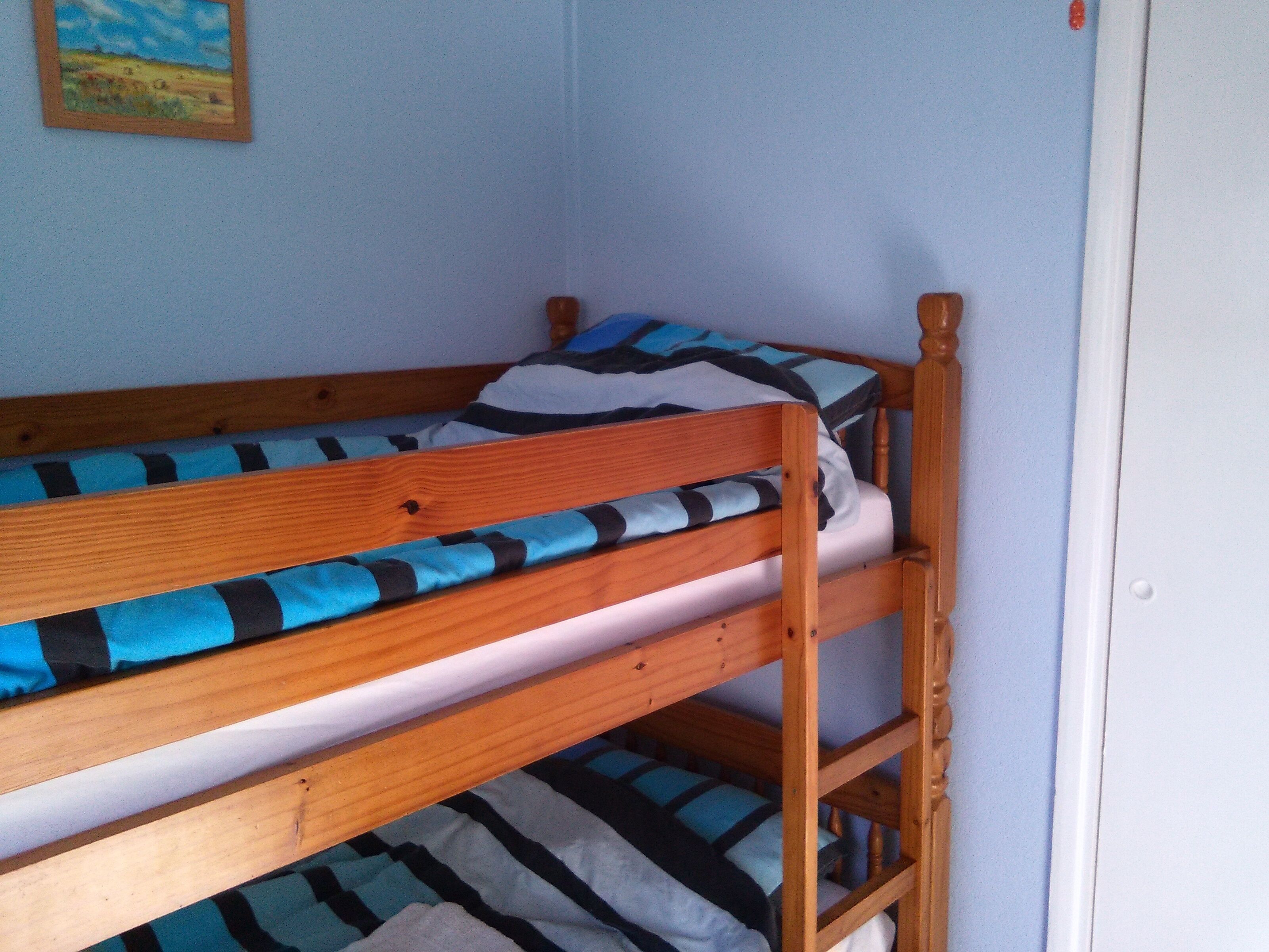 Ein Stockbett mit blau-schwarz gestreifter Bettwäsche, einem Holz-Kopfteil und einem kleinen Bild an der Wand.