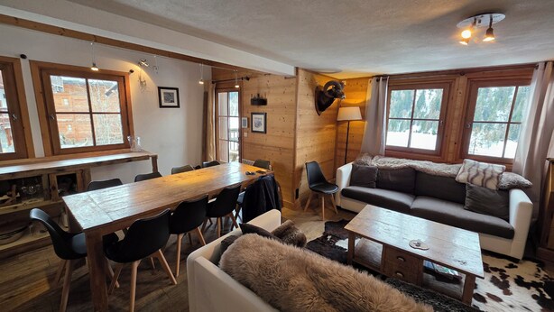A cozy cabin interior with a wooden dining table, a sofa, and a lamp. - Typical chalet, combining the charm of wood and stone, overlooking the Isère river  (Tignes)
