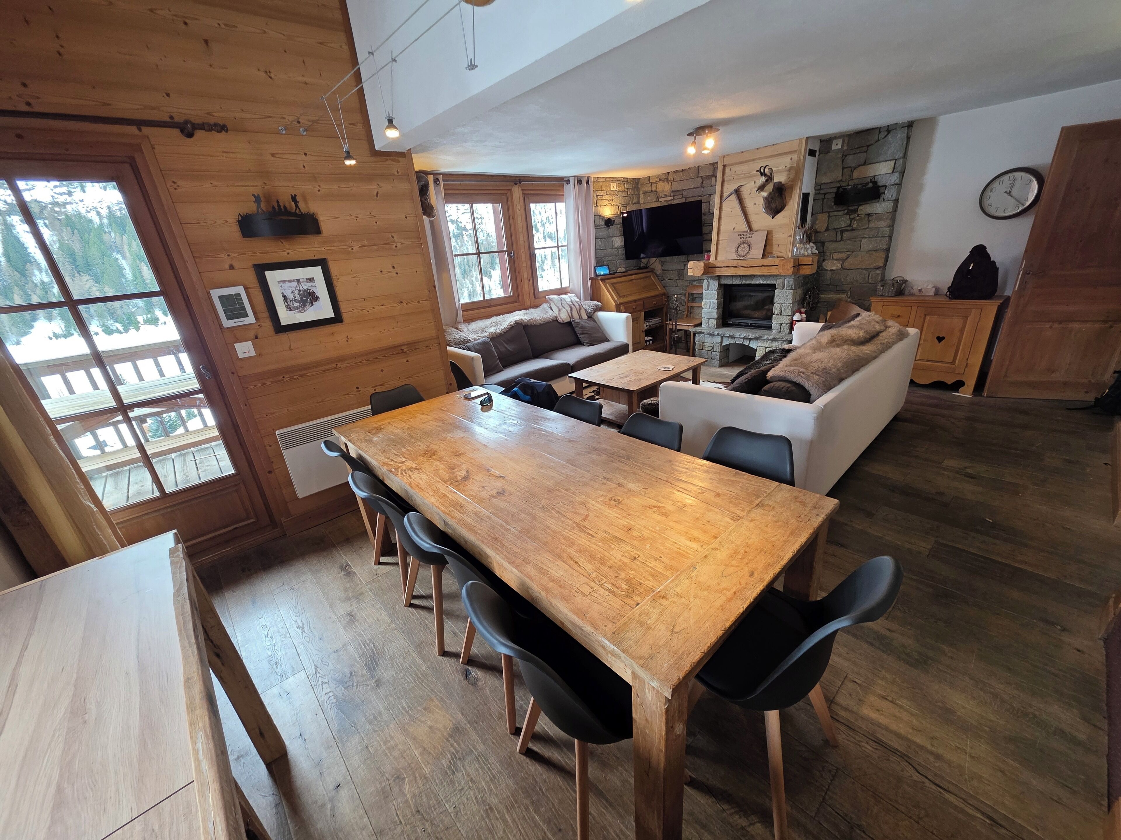 Ein Holzinterieur mit Esstisch, Stühlen, einer Couch und einem Kamin aus Stein.