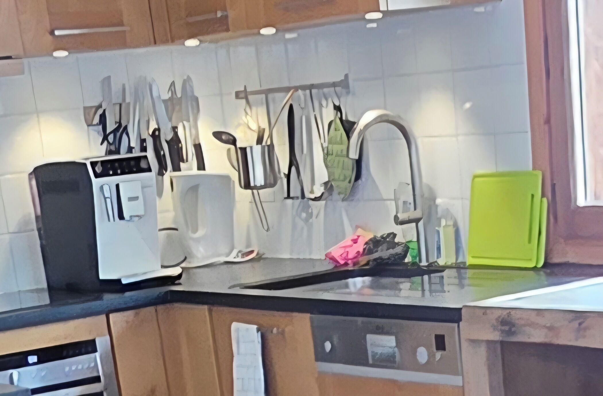 Eine Küche mit Holzausstattung, einer schwarzen Arbeitsplatte, einem weißen Toaster, einer grünen Schneidebrett und verschiedenen Küchenutensilien, die an einem Gestell hängen.