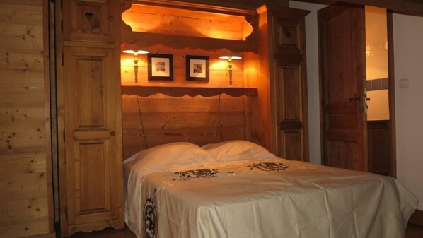 A wooden cabin-style bedroom with a bed, wooden walls, and a ceiling with framed pictures.