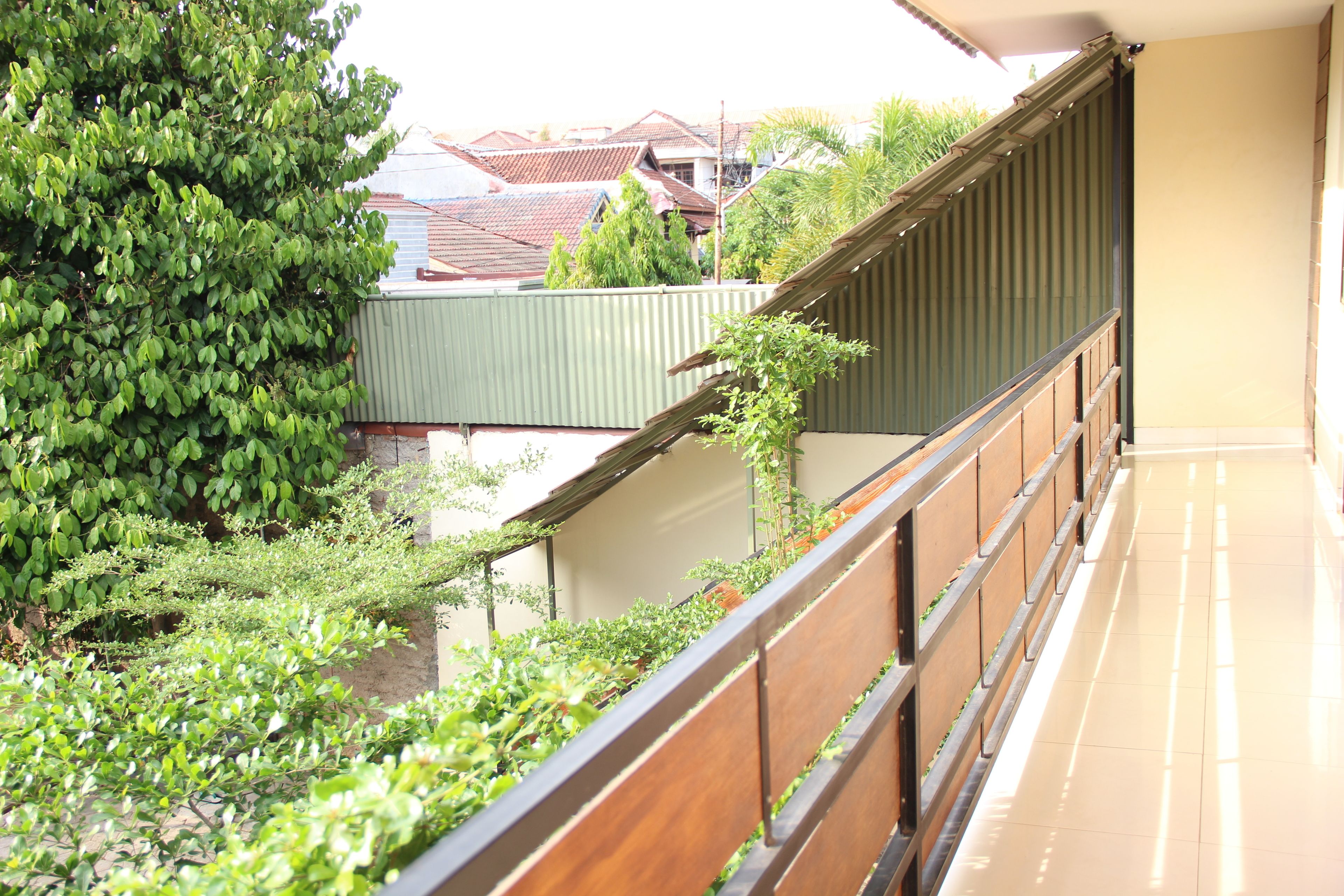 A balcony with a wooden railing overlooking a garden and neighboring buildings.