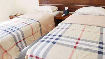 Una habitación de hotel con dos camas, cada una con colcha de cuadros, cabecero de madera, mesita de noche con lámpara y teléfono.