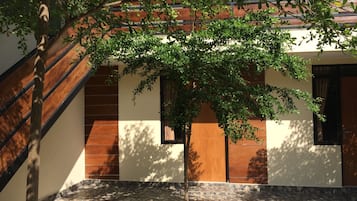 A building with a tiled courtyard, wooden steps, and a tree providing shade.