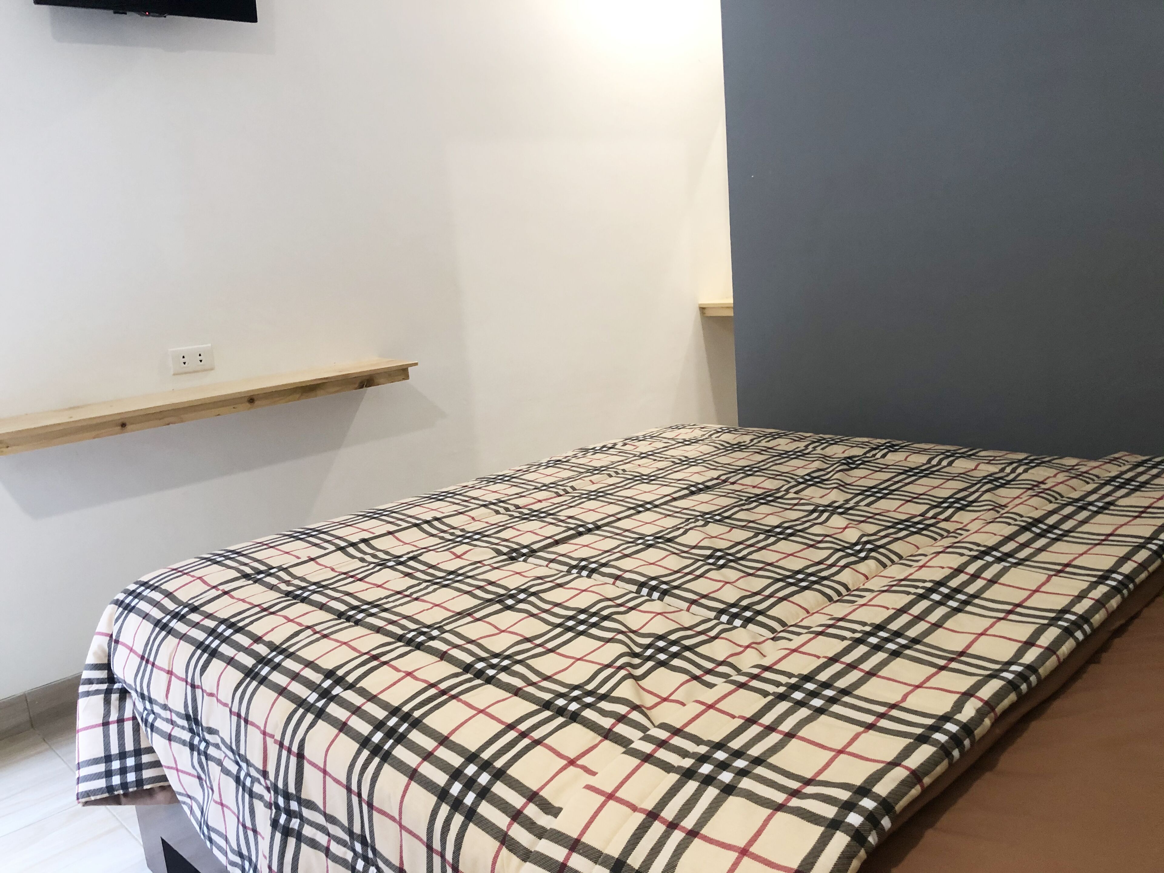 Une chambre à coucher avec un lit, une étagère en bois et un téléviseur fixé au mur.